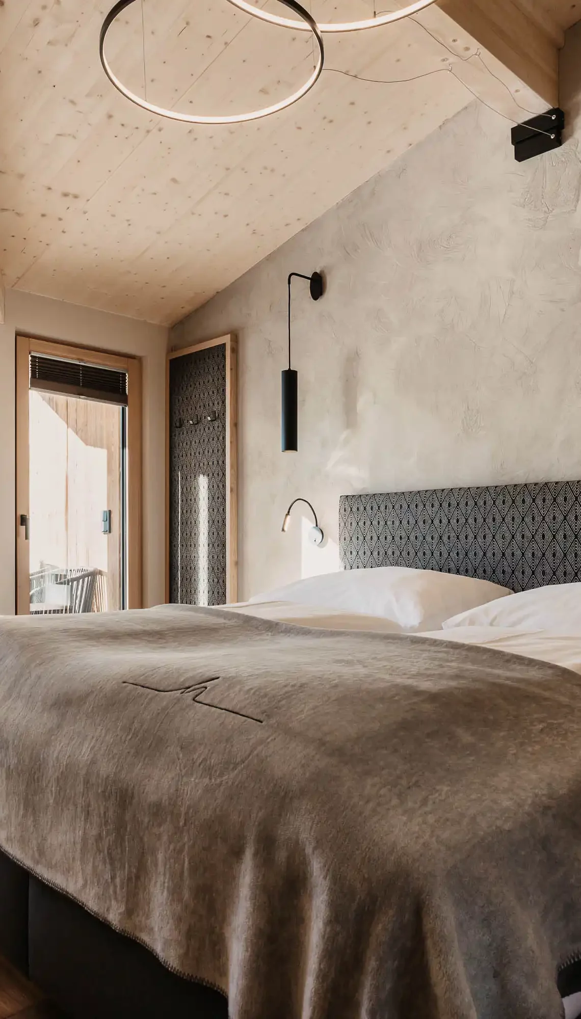 Modern eingerichtetes Schlafzimmer mit gemütlichem Doppelbett, freistehender Badewanne vor bodentiefem Fenster und stilvollem Holzdach – alpiner Luxus mit Panoramablick.