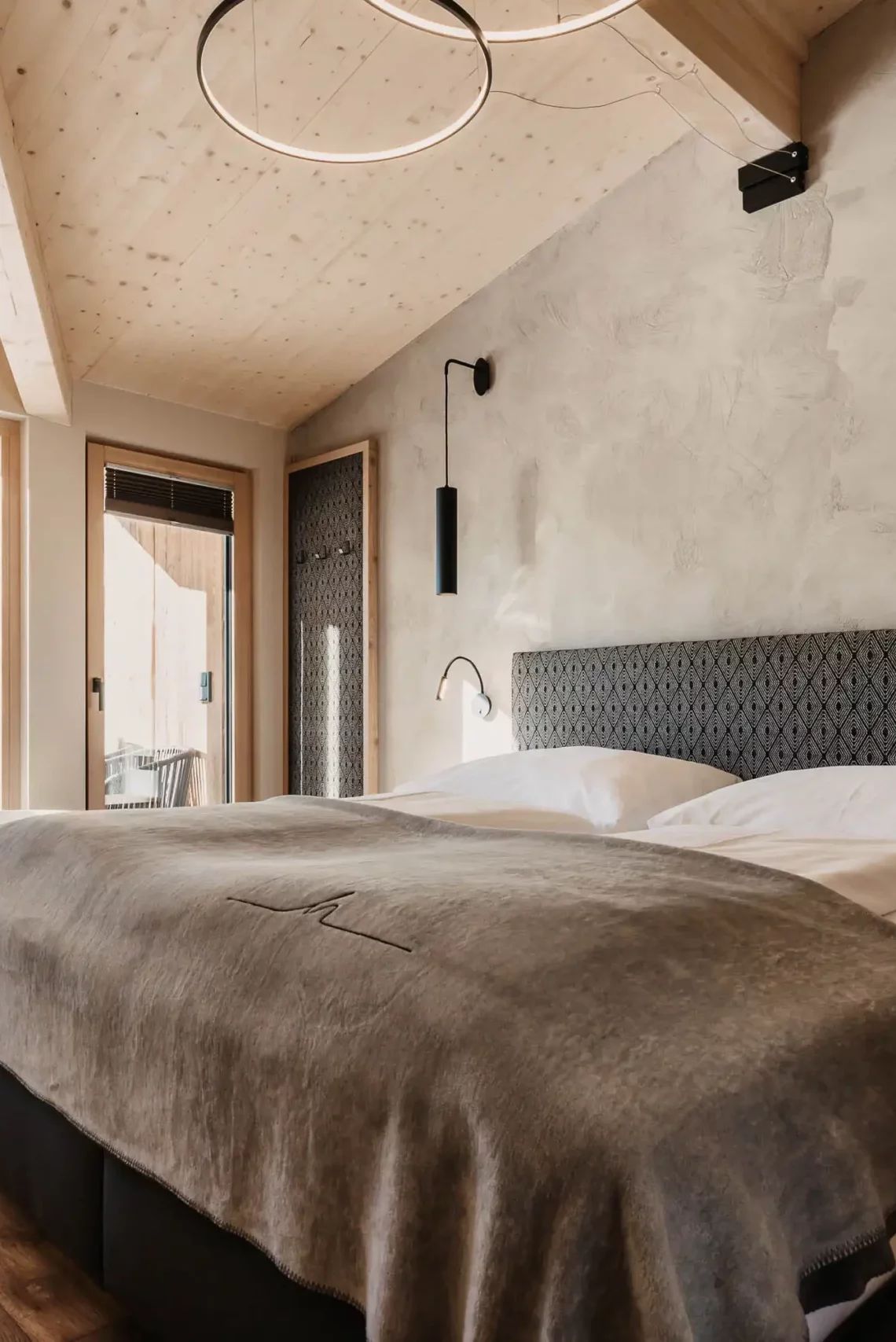 Modern eingerichtetes Schlafzimmer mit gemütlichem Doppelbett, freistehender Badewanne vor bodentiefem Fenster und stilvollem Holzdach – alpiner Luxus mit Panoramablick.