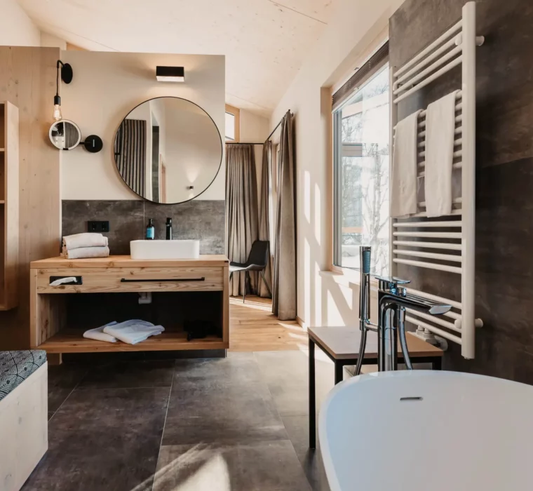 Modernes Design trifft alpinen Charme – Ihr stilvolles Badezimmer im Hofgut Wagrain mit warmen Holzakzenten und Blick in die Natur.