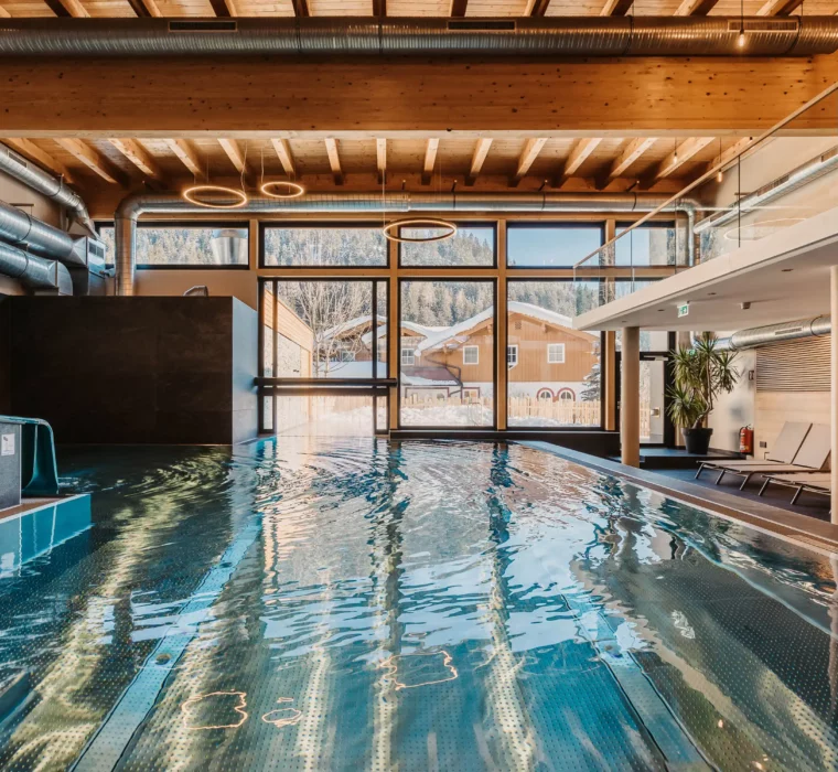 Stimmungsvolle Aufnahme des Indoor-Pools im Hofgut Wagrain mit Blick ins verschneite Tal – wohltuende Wärme, modernes Design und ein einzigartiger Ort zum Innehalten.