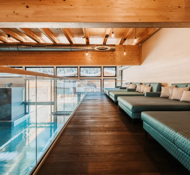 Ruhige Wellnesslounge mit gemütlichen Liegen und Blick auf den Indoorpool im Hofgut Wagrain.