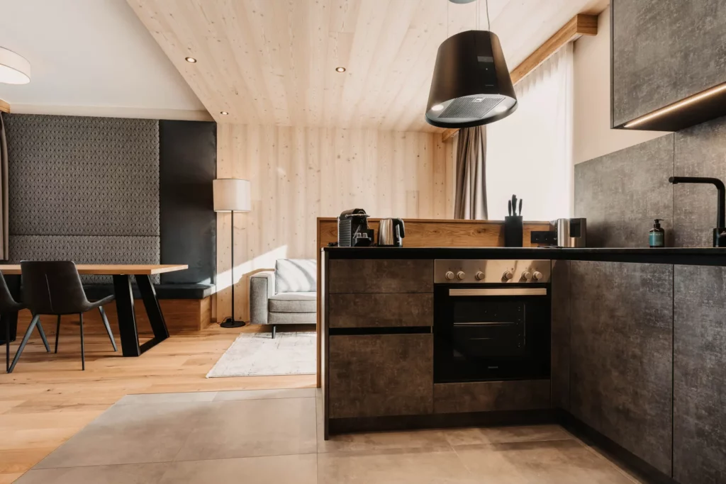 Moderne Apartment-Küche im Hofgut Wagrain mit hochwertigen Geräten, dunklen Fronten in Betonoptik und stilvollen Holzelementen. Offenes Wohnkonzept mit gemütlicher Essecke und alpinem Design.