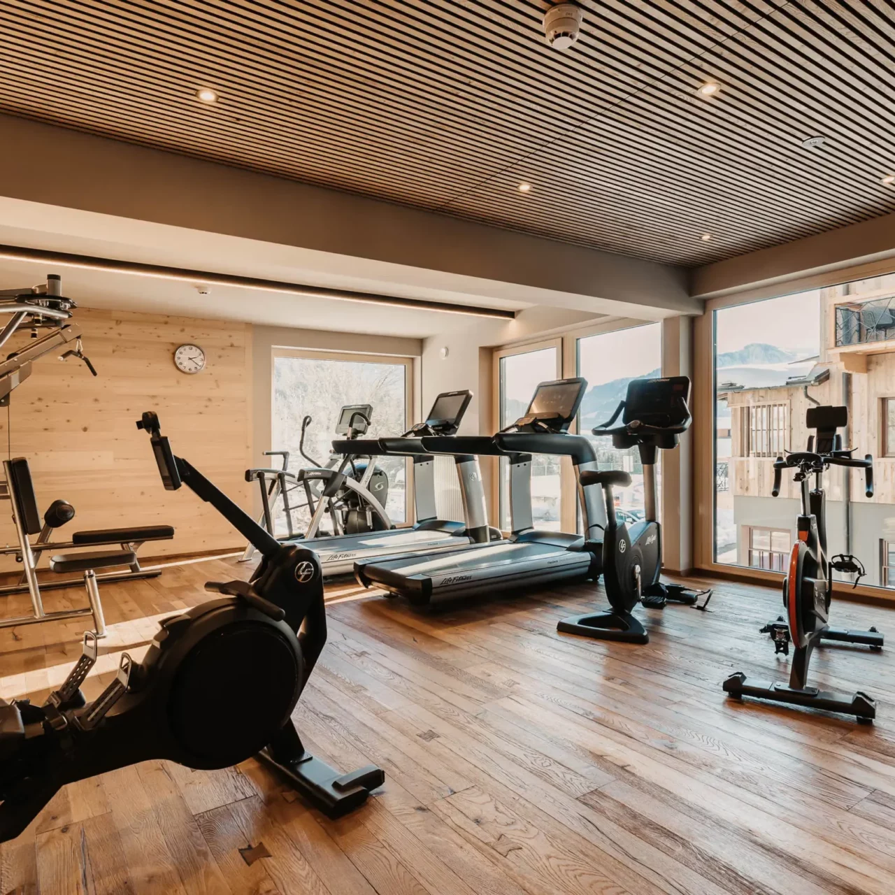 Modern fitness studio in Hofgut Wagrain with high-quality equipment, wooden design and a view of the snow-covered mountains.
