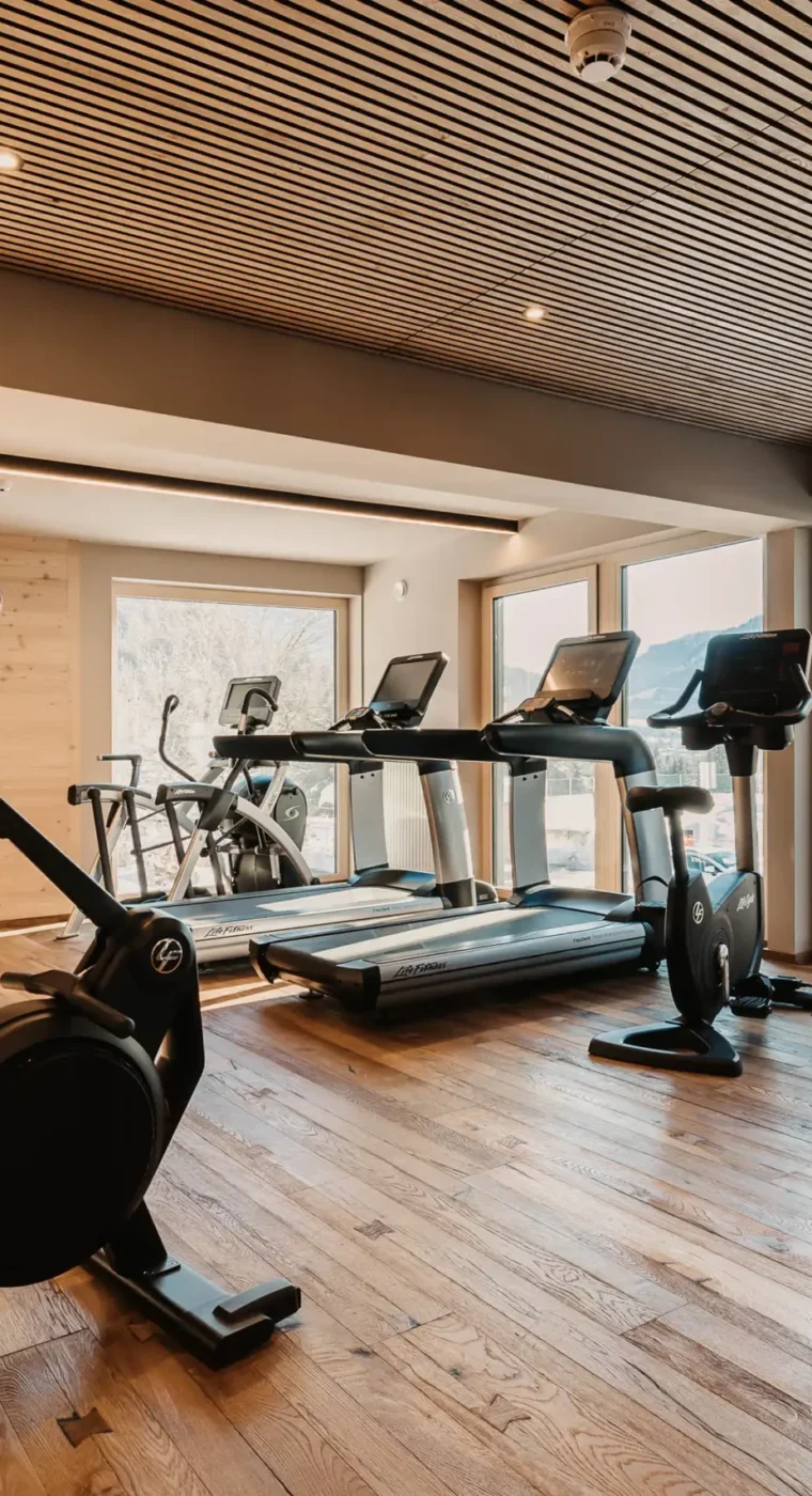 Modernes Fitnessstudio im Hofgut Wagrain mit hochwertigen Geräten, Holzdesign und Blick auf die verschneiten Berge.