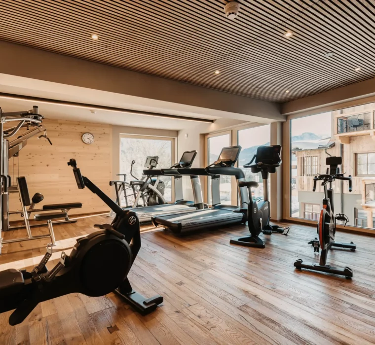 Modernes Fitnessstudio im Hofgut Wagrain mit hochwertigen Geräten, Holzdesign und Blick auf die verschneiten Berge.