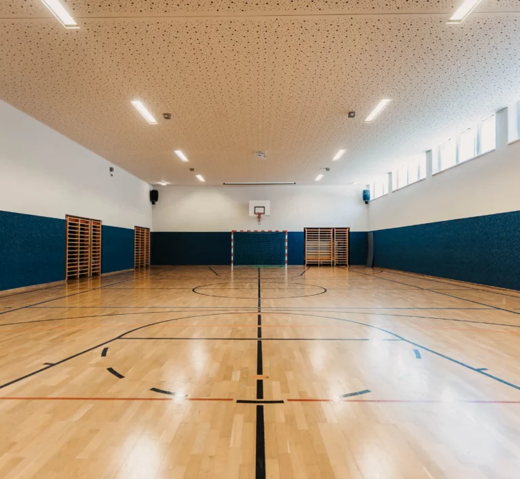 Large, bright sports hall at Hofgut Wagrain with wooden floor, basketball hoop and goal - ideal for indoor sports and exercise.