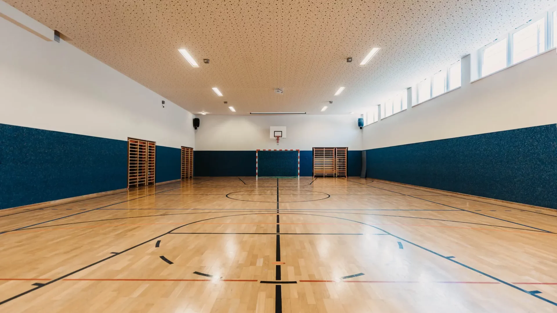 Large, bright sports hall at Hofgut Wagrain with wooden floor, basketball hoop and goal - ideal for indoor sports and exercise.
