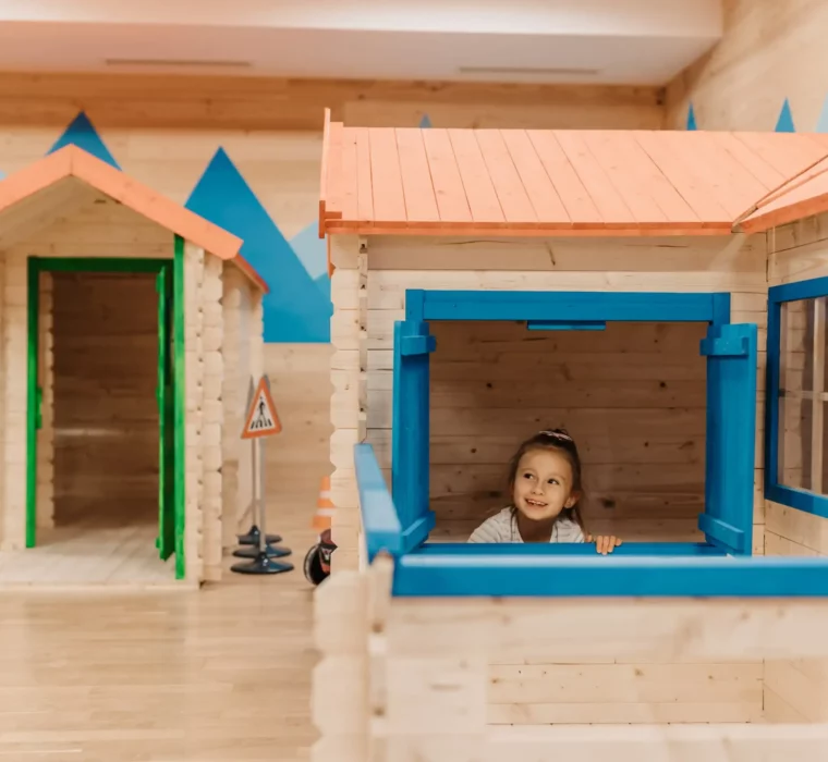 Kleine Häuser, große Abenteuer: Strahlende Kinderaugen im liebevoll gestalteten Mini-Marktplatz des Hofgut Wagrain – Spielen, Entdecken und Träumen in sicherer Umgebung.