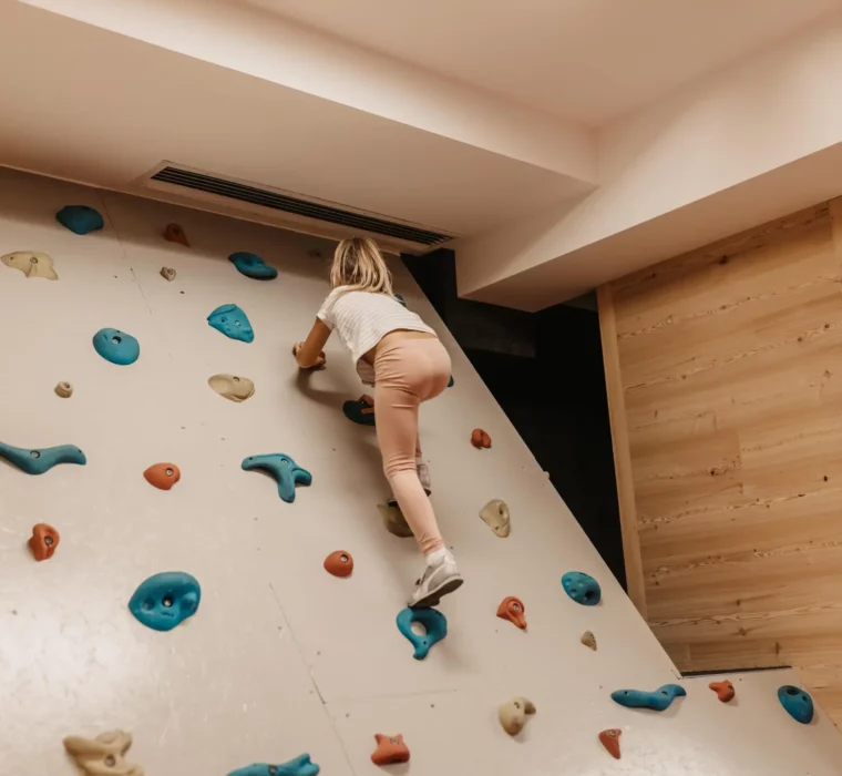 Ein kleines Kind erklimmt mutig die Indoor-Kletterwand im Hofgut Wagrain – voller Energie, Entdeckerfreude und kindlichem Stolz.
