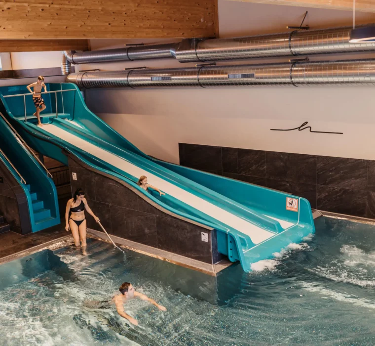 Swimming fun for the whole family in the warm indoor pool with slide - shared laughter and lightness at Hofgut Wagrain.