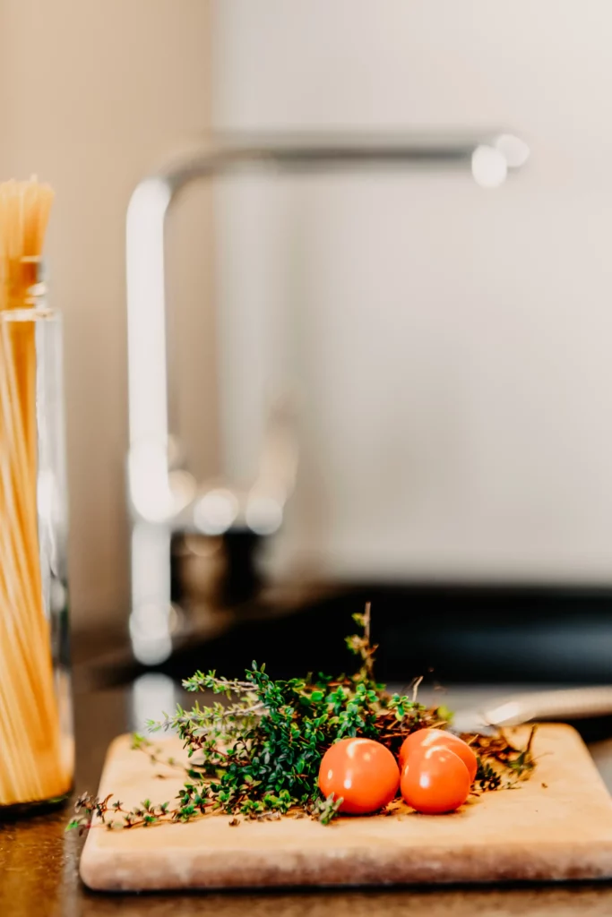 Fresh cocktail tomatoes and herbs on a wooden board in a modern flat kitchen with pasta in the background