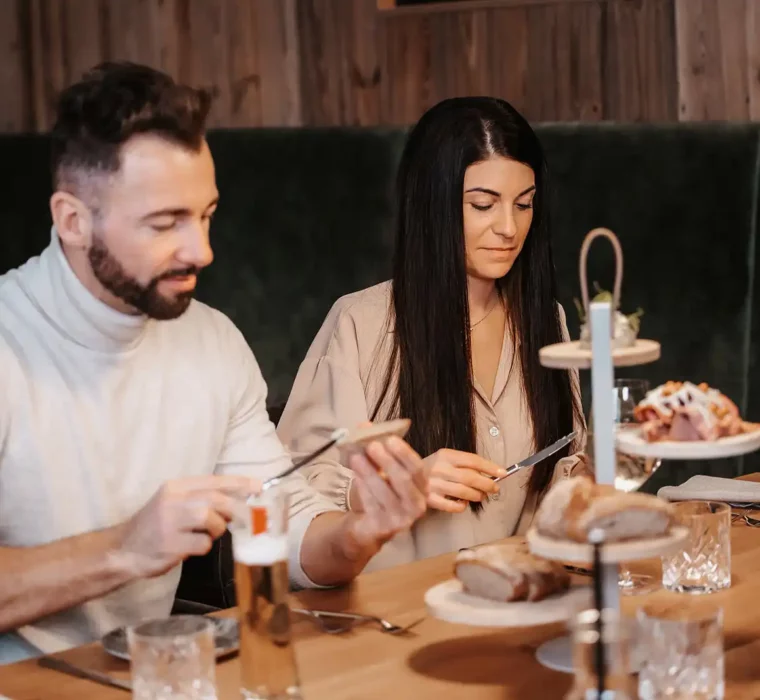 A couple sit together in a restaurant and reach for bread while smiling and looking at each other.