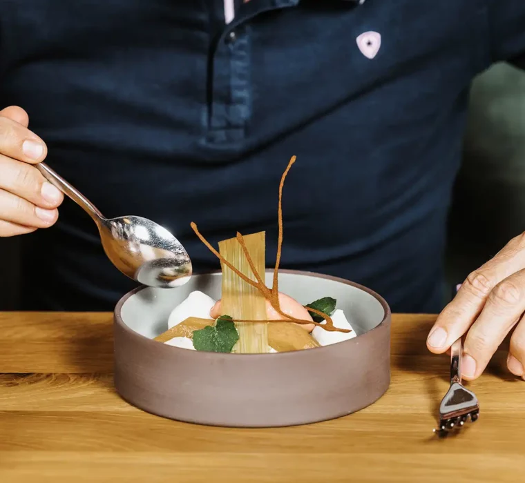 A guest sits at the table and enjoys dessert with a spoon and fork.