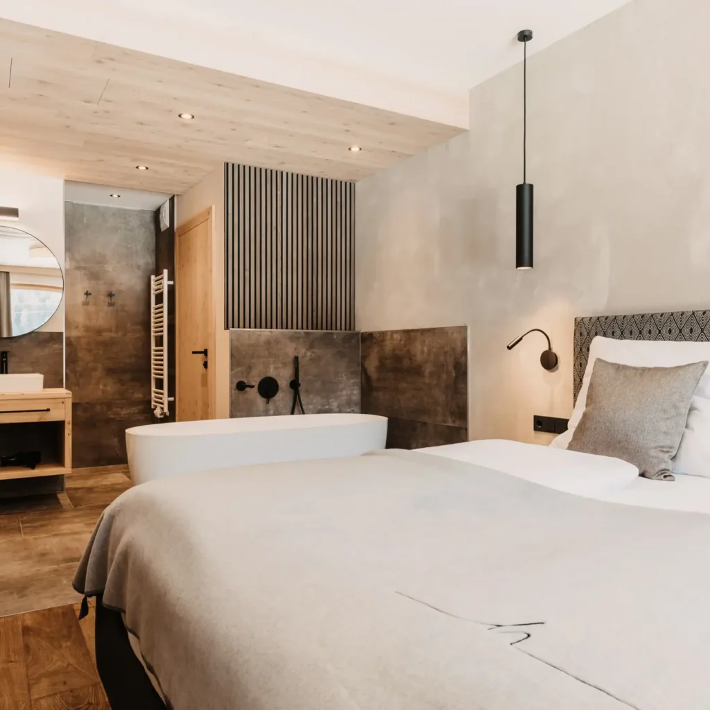 Bright bedroom at Hofgut Wagrain with cosy double bed and open bathroom with free-standing bathtub.