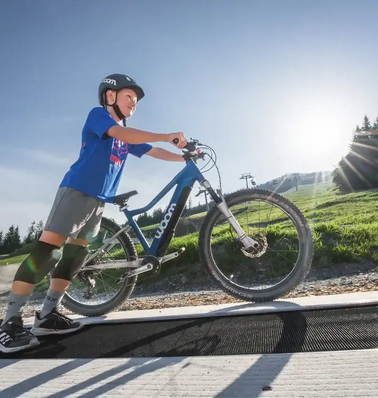 Junge mit Mountainbike auf Förderband im Bikepark bei Sonnenschein im Salzburger Land