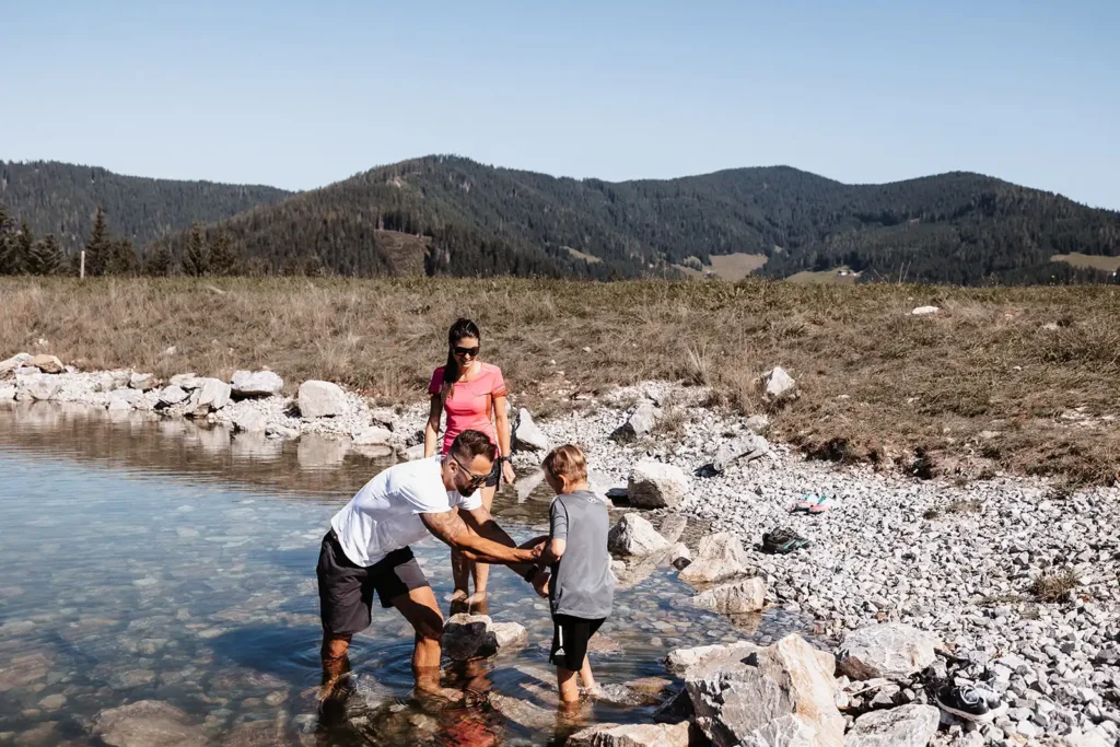 Familie genießt barfuß das klare, kühle Wasser eines alpinen Baches - Naturerlebnis für Groß und Klein.
