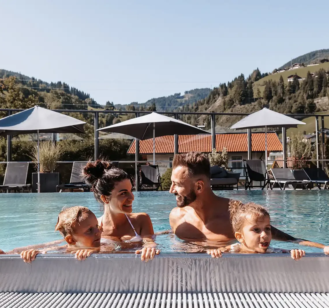 Glückliche Familie entspannt im Rooftopool des Hofgut Wagrain mit Panoramablick auf die Berge.