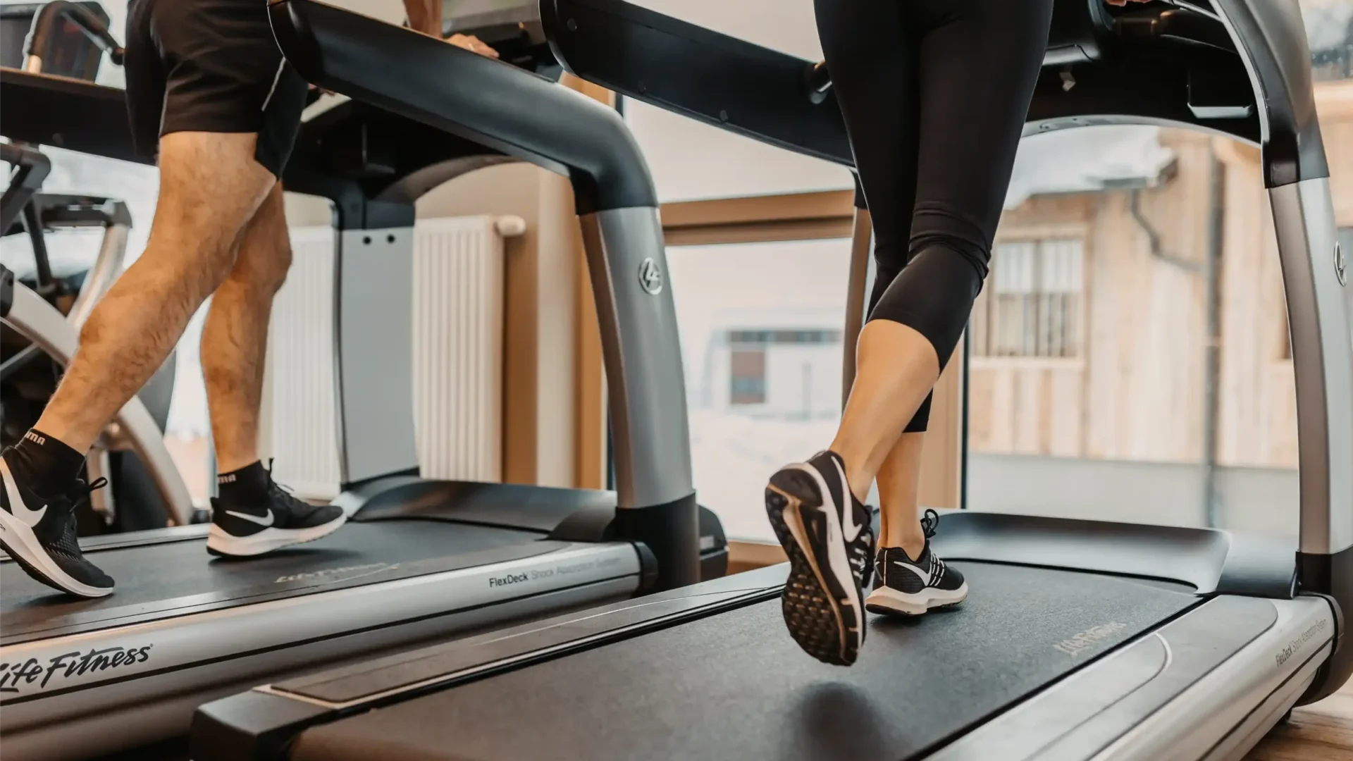 Aktiv entspannen im Urlaub: Zwei Gäste trainieren motiviert im lichtdurchfluteten Fitnessbereich des Hofgut Wagrain – umgeben von hochwertigem Holzambiente und modernsten Geräten.