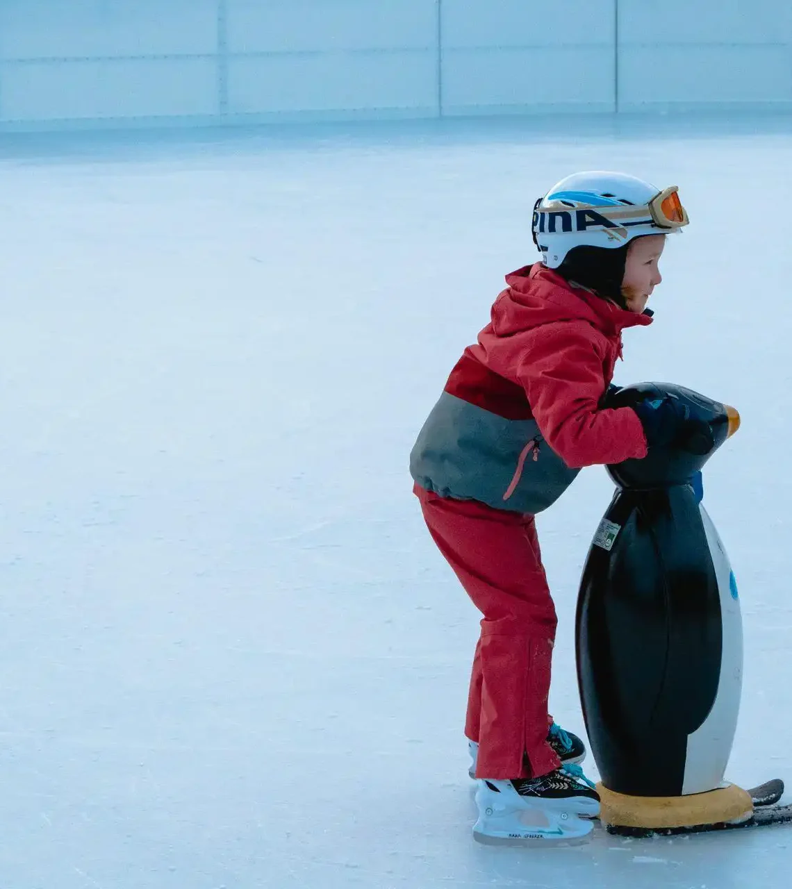 Ein Kind läuft auf einer Eisfläche am Eislaufplatz Wagrain und hält sich an einer Pinguin-Laufhilfe fest.