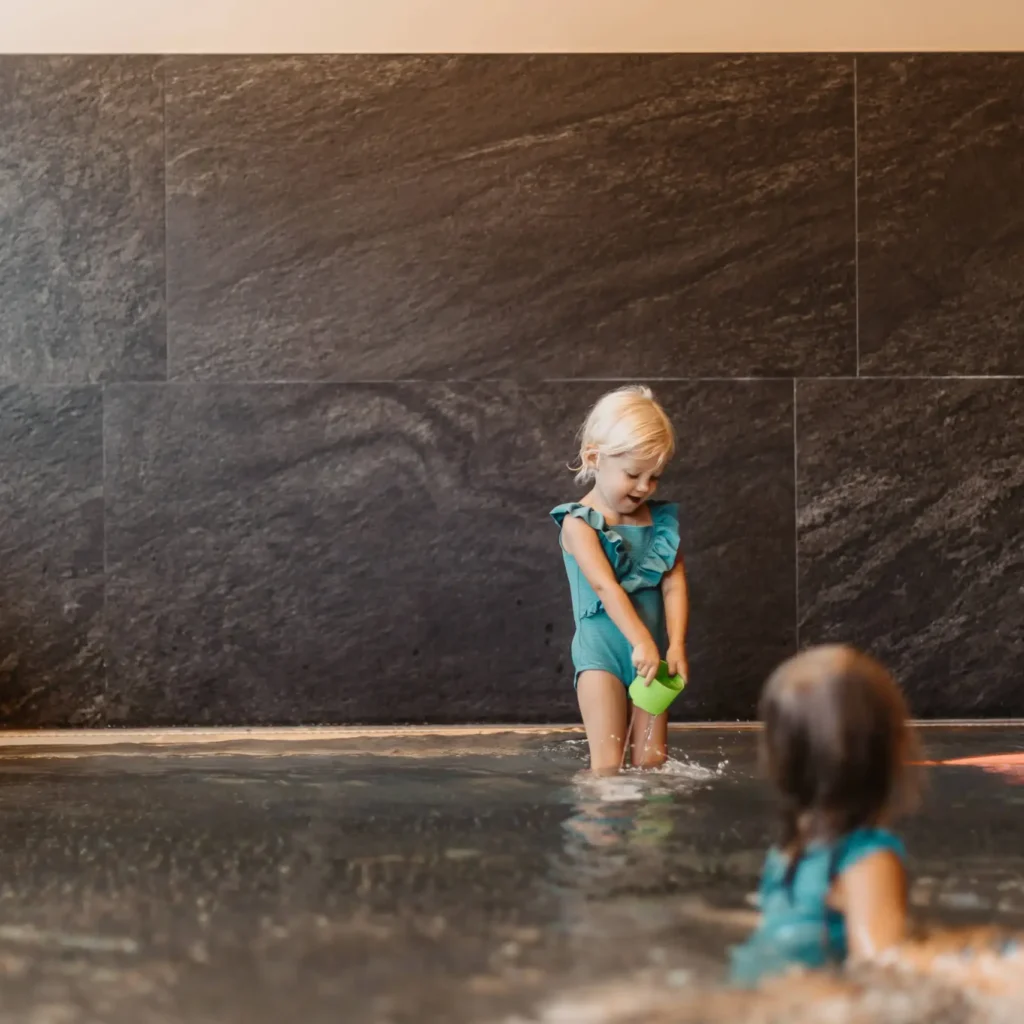 Zwei kleine Kinder spielen fröhlich im Babypool mit Wasser und Spielzeug.