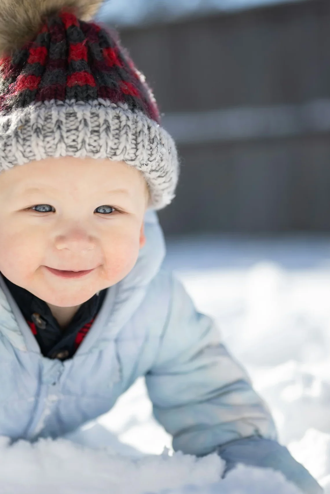 Ein lächelndes Kleinkind in Winterkleidung spielt im frischen Schnee.