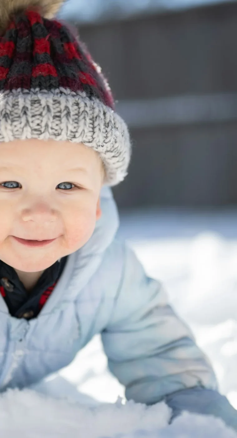 Ein lächelndes Kleinkind in Winterkleidung spielt im frischen Schnee.
