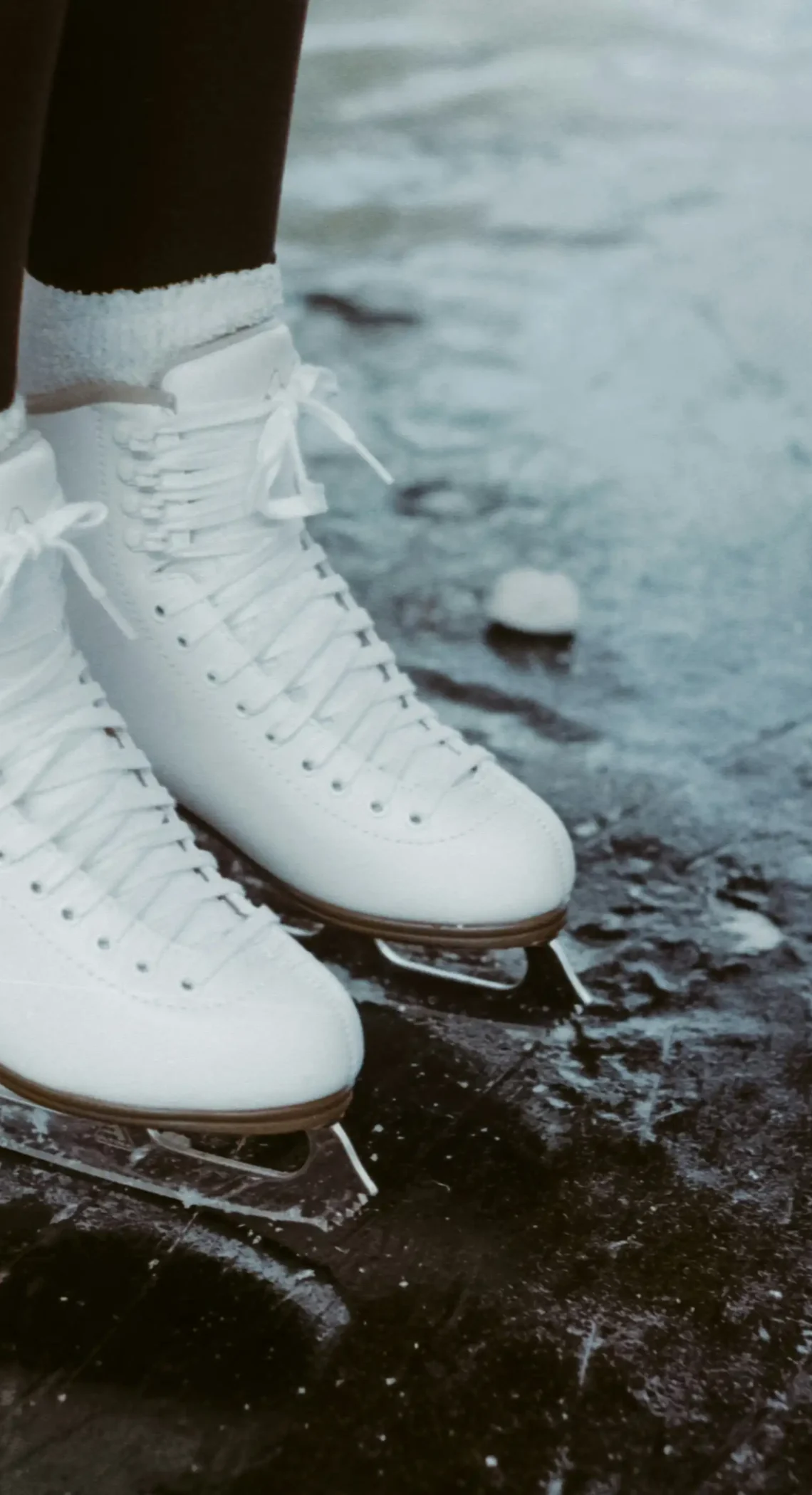 Weiße Eislaufschuhe stehen auf einer leicht zerkratzten Eisfläche.