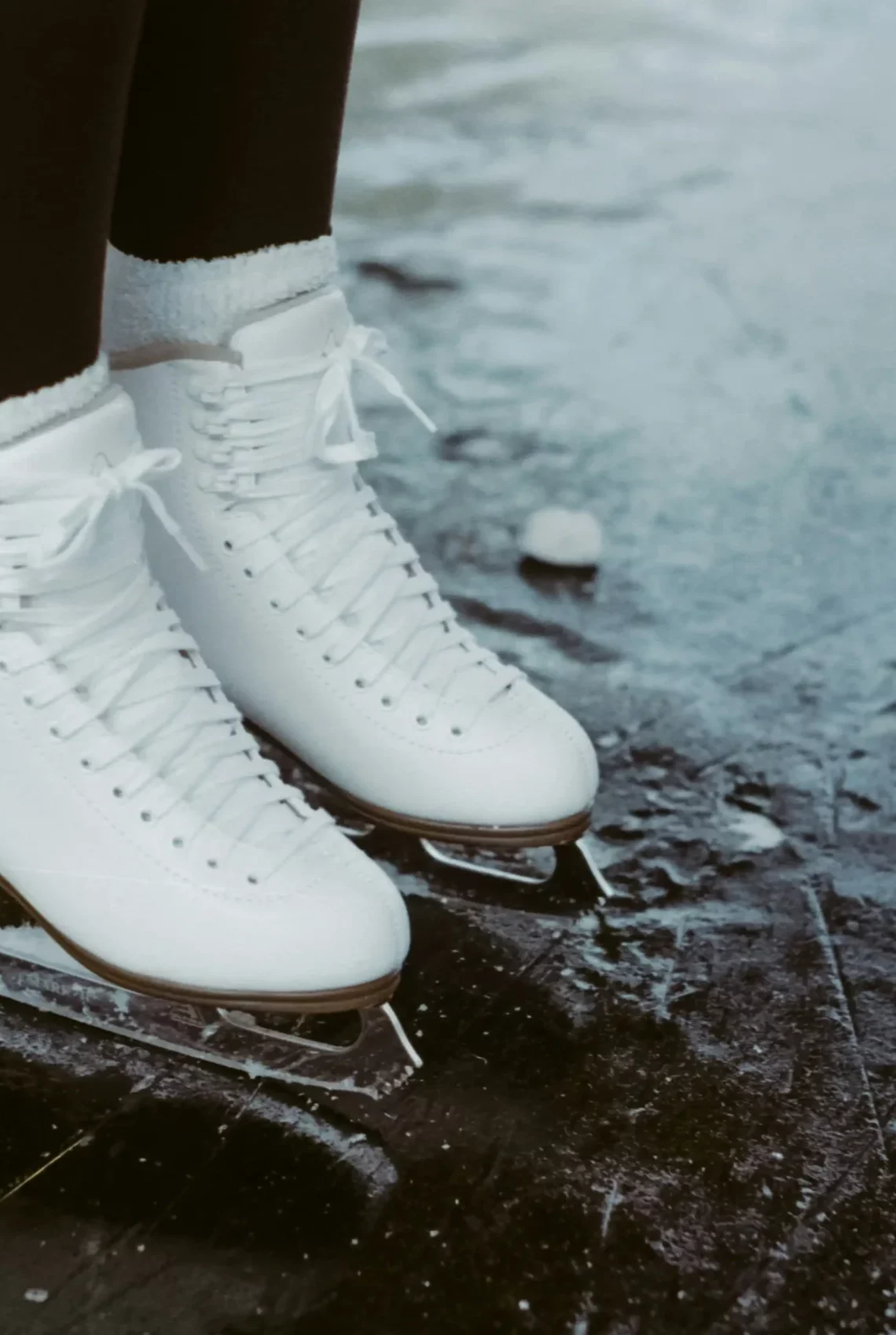 Weiße Eislaufschuhe stehen auf einer leicht zerkratzten Eisfläche.