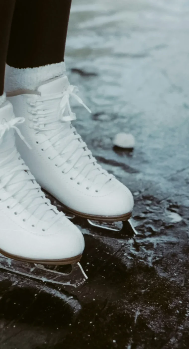 Weiße Eislaufschuhe stehen auf einer leicht zerkratzten Eisfläche.