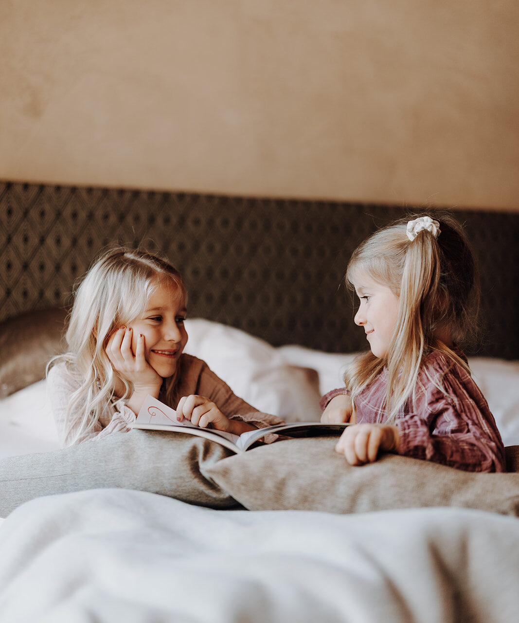 Zwei glückliche Kinder lesen gemeinsam ein Buch im gemütlichen Apartment des Hofgut Wagrain und genießen eine entspannte Familienzeit im stilvollen Schlafzimmer
