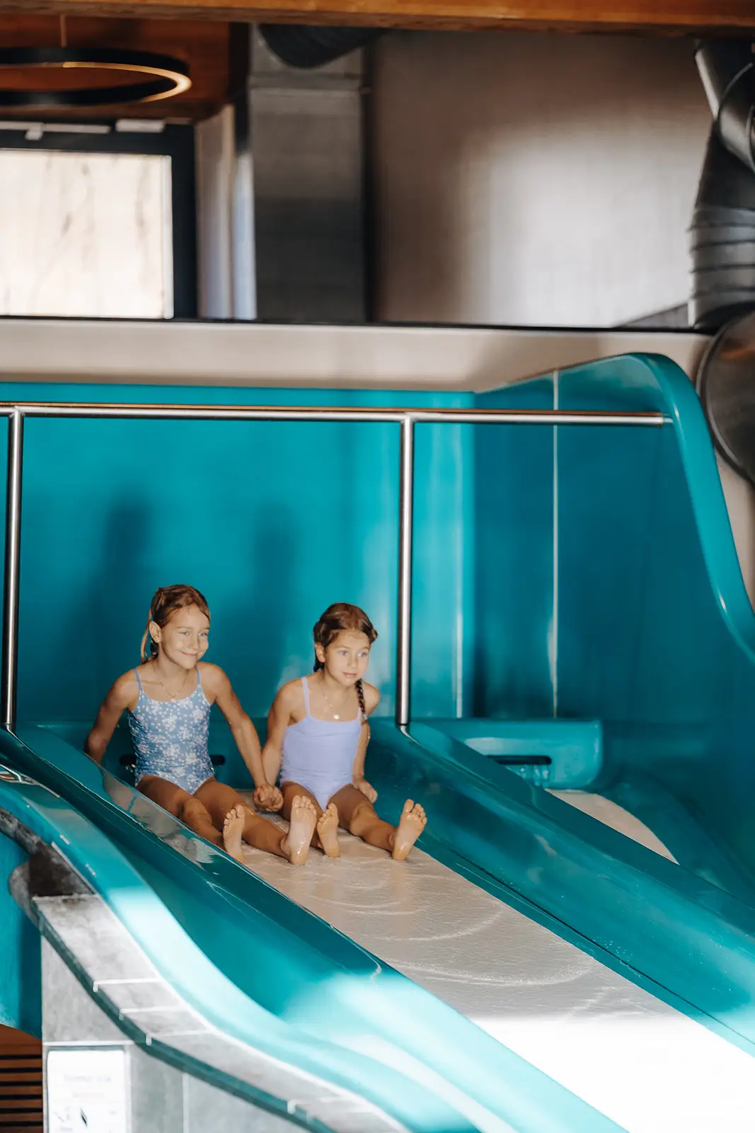 Zwei Kinder sitzen nebeneinander am Start der Wasserrutsche im Hallenbad des Hofgut Wagrain.