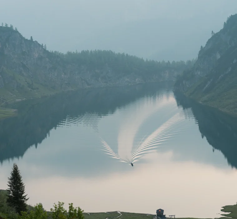 Bergsee Tappenkarsee in Wagrain-Kleinarl mit kleinem Boot auf dem Wasser und nebeliger Alpenkulisse im Hintergrund.