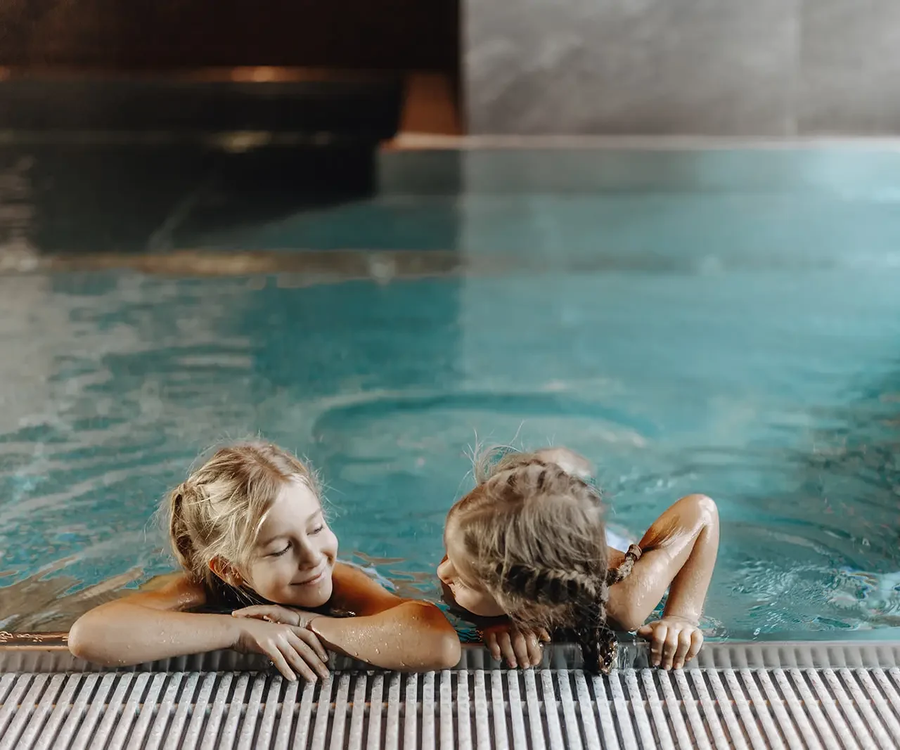 Two children hold onto the edge of the indoor pool at Hofgut Wagrain.