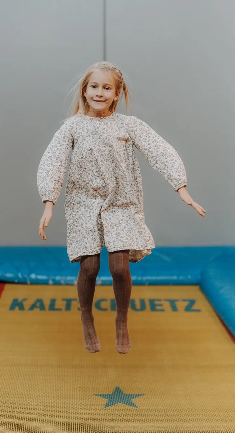 Et barn hopper højt på trampolinen i den indendørs legeverden på Hofgut Wagrain.